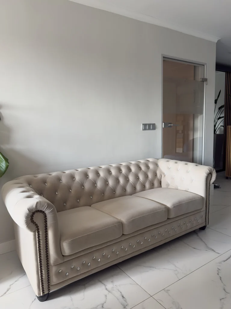 Jasna pikowana sofa z ozdobnymi guzikami i tapicerowanymi podłokietnikami